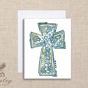 May include: A white greeting card featuring a teal and gold cross design with floral accents. The cross is centered on the card, with a matching white envelope behind it. The Paisley Label Co. logo is in the lower left corner.