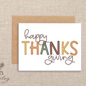 May include: Thanksgiving greeting card with a white background and a brown envelope. The card features the words "happy THANKSgiving" in various colors and fonts. The Paisley Label Co. logo is in the bottom left corner.