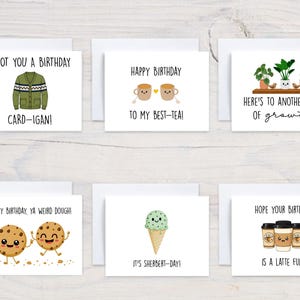 May include: A collection of birthday greeting cards with various designs. One card features a green cardigan illustration with the text "I GOT YOU A BIRTHDAY CARD-IGAN!". Other cards have illustrations of tea cups, cookies, ice cream, and coffee cups.