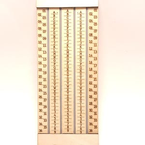 May include: A rectangular light-colored wooden tool featuring three vertical columns. The outer columns display numbers from 01 to 36, while the two central columns contain the alphabet from A to Z followed by the numbers 0 through 9 in a vertical sequence.
