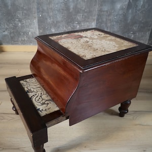 May include: A dark wood step stool with a rectangular top and a single step. The top and step are inlaid with patterned fabric. The stool has four turned legs and a curved side.