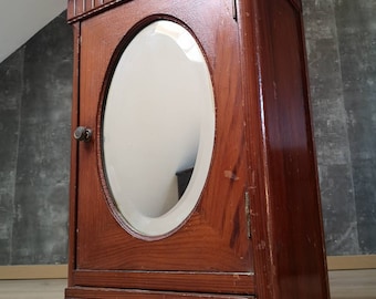 May include: A vintage wooden wall cabinet with an oval mirror and a single drawer. The cabinet is painted a dark brown color and has a simple design.