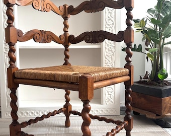 May include: Antique wooden chair with a woven seat. The chair features intricately carved details and twisted legs and supports. The backrest has a curved design. The chair is made of a warm brown wood.