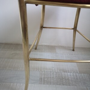 May include: A gold metal chair with a burgundy velvet seat. The chair has a simple, elegant design with a curved back and straight legs.