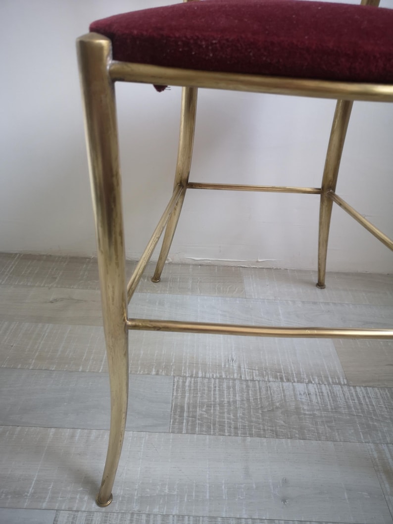 May include: A gold metal chair with a burgundy velvet seat. The chair has a simple, elegant design with a curved back and straight legs.