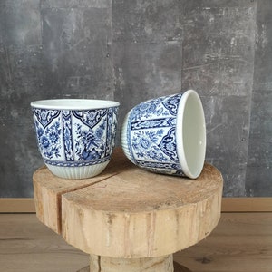 May include: Two blue and white ceramic planters with a floral design. The planters are sitting on a wooden stump.