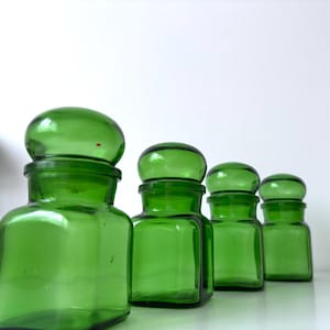 Peut inclure: Quatre bocaux d'apothicaire en verre vert avec des couvercles arrondis. Les bocaux sont disposés en rangée, de taille décroissante. Les bocaux ont une base carrée et un dessus arrondi. Les bocaux sont d'un vert vif.