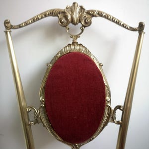 May include: A gold-toned metal stand with a red velvet cushion. The stand has a decorative, ornate design and is shaped like a chair.