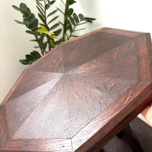Könnte beinhalten: Ein dunkelbrauner, achteckiger Beistelltisch aus Holz mit einem geometrischen Design auf der Tischplatte. Der Tisch hat einen satten, warmen Farbton und sichtbare Holzmaserung. Die Beine sind kurz und stabil, und der Tisch steht vor einem neutralen Hintergrund.