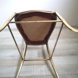 May include: A gold metal chair with a red velvet seat. The chair has a simple, modern design with a curved back and slender legs.