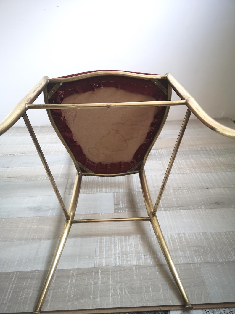 May include: A gold metal chair with a red velvet seat. The chair has a simple, modern design with a curved back and slender legs.