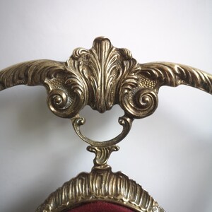 May include: A gold-tone chair with a red velvet seat and ornate scrollwork details. The chair has a high back and a curved frame.