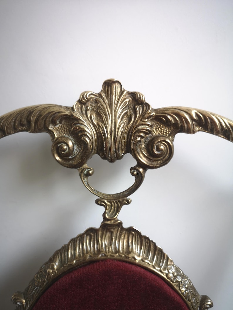 May include: A gold-tone chair with a red velvet seat and ornate scrollwork details. The chair has a high back and a curved frame.
