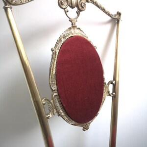 May include: A gold-tone chair with a red velvet seat and ornate brass detailing. The chair has a high back with a curved top and a decorative design.