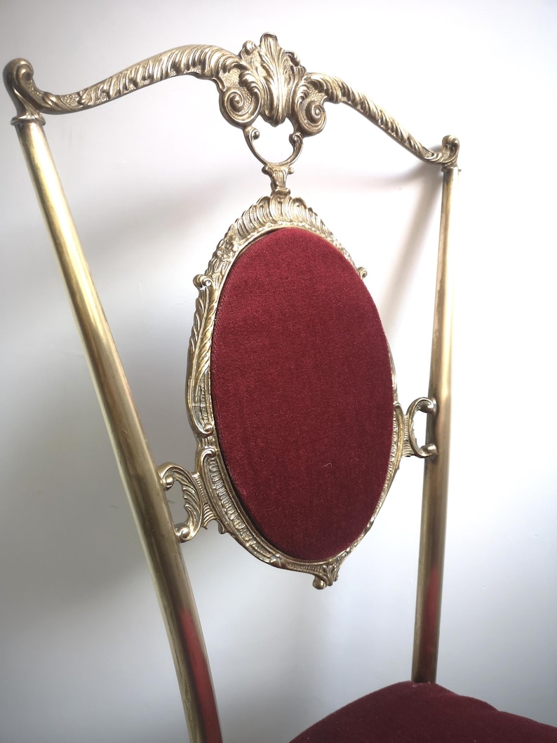 May include: A gold-tone chair with a red velvet seat and ornate brass detailing. The chair has a high back with a curved top and a decorative design.