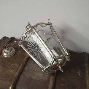 May include: A silver hanging lantern with a clear glass shade featuring a starburst pattern. The lantern is hanging from a chain and has a decorative metal top.