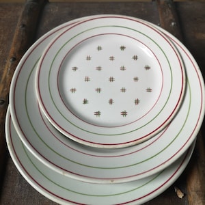 May include: Three white ceramic plates with green and red trim. The smallest plate has a pattern of red and green crosses.