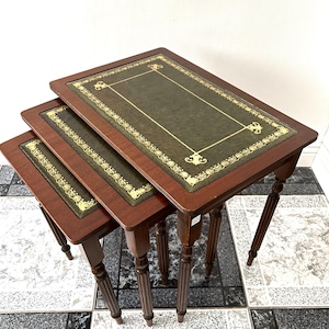 Op de afbeelding: Set van drie nesttafels met donkerhouten frames en groene leren bladen. Het leer is afgewerkt met gouden randen. De tafels hebben decoratieve poten en zijn in een geneste configuratie gerangschikt.