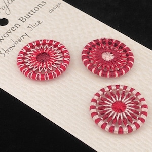 May include: Three handwoven buttons in the "Strawberry Slice" design. Each button is approximately 1 inch in diameter, featuring a red and white woven pattern. The buttons are displayed on a white card with the maker's name.