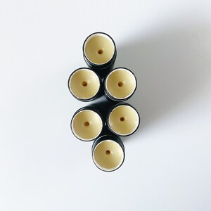 May include: Seven black and white lip balm tubes with a yellow balm inside. The tubes are arranged in a pyramid shape.
