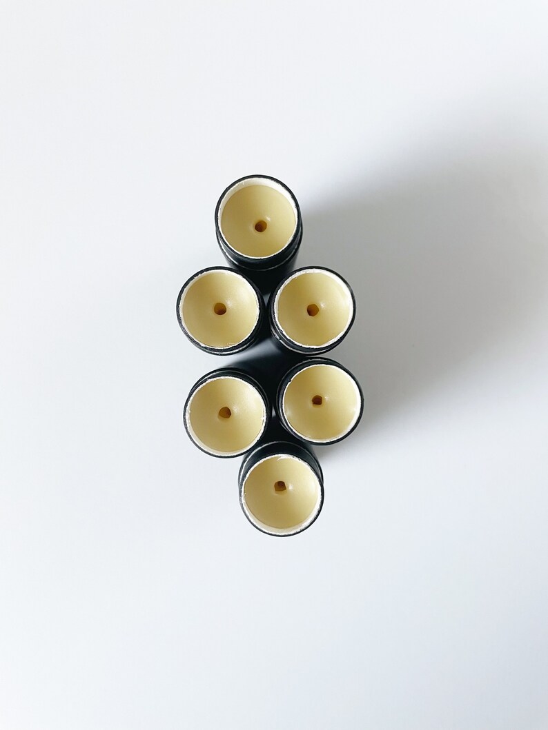 May include: Seven black and white lip balm tubes with a yellow balm inside. The tubes are arranged in a pyramid shape.