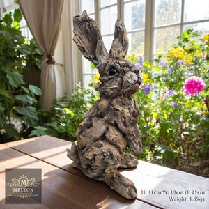 May include: A detailed, realistic sculpture of a rabbit made from driftwood. The rabbit is sitting up with its ears perked up and its eyes open. The sculpture is painted in shades of brown and grey to resemble natural wood. The sculpture is 41 cm tall, 19 cm wide, and 21 cm deep and weighs 1.5 kg.