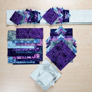 Blue, purple and grey print batiks cut into squares, rectangles and strip and stacked by size and shape.