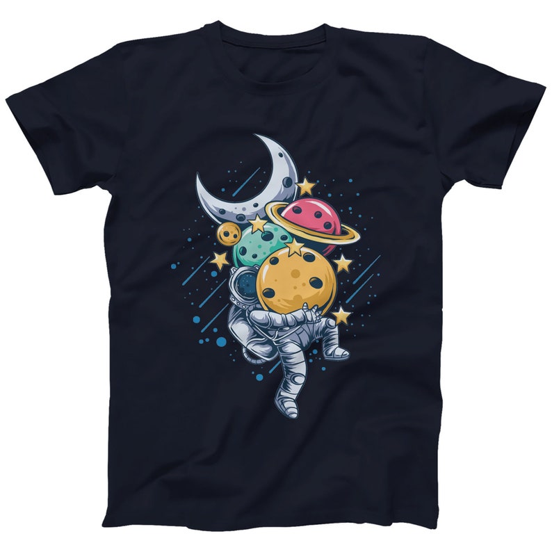 Op de afbeelding: Een marineblauw t-shirt met een cartoonillustratie van een astronaut die een groep planeten en een halve maan vasthoudt. De planeten zijn geel, groen, roze en blauw.