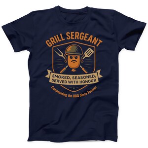 May include: Navy blue t-shirt with a humorous graphic. The design features a cartoon sausage wearing a helmet, crossed grilling tools, and the text "GRILL SERGEANT". Below, it reads "SMOKED, SEASONED, SERVED WITH HONOUR" and "Commanding the BBQ Since Forever".