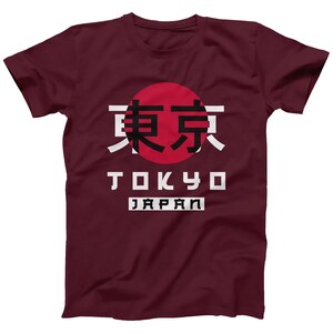 May include: A maroon t-shirt with a white graphic design featuring the Japanese characters for Tokyo, the word "Tokyo" in white block letters, and the word "Japan" in white block letters. The graphic also includes a red circle with a white outline.