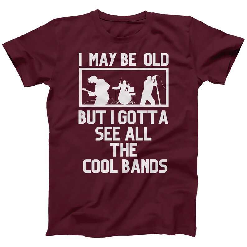 K&ouml;nnte beinhalten: Burgunderfarbenes T-Shirt mit wei&szlig;em Text, der "I may be old but I gotta see all the cool bands" lautet. Der Text ist von einem wei&szlig;en Rechteck umgeben. Im Inneren des Rechtecks befindet sich eine Silhouette einer Band, die Musik spielt.
