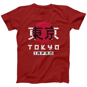 May include: Red t-shirt with a white circle and black Japanese characters that say "Tokyo" in English below the circle. The words "Japan" are printed in white below the word "Tokyo".