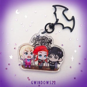 May include: A clear acrylic keychain with three cartoon characters from Nevermore Academy. The keychain has a black bat-shaped clasp. The characters are in pink, red, and black outfits. The text "GWINDOWS22" is at the bottom of the keychain.