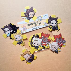 Può includere: Una collezione di adesivi colorati con personaggi dei cartoni animati con tratti simili a quelli dei gatti. Gli adesivi sono disposti su una superficie arancione chiaro. Il testo "THUNDERBOLT KITTIES!" e "6 PCS" è visibile su un'etichetta bianca.