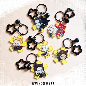 May include: A collection of character keychains featuring various cartoon figures. Each keychain has a yellow cross-shaped base with a character image, a black star-shaped charm, a black ball, and a keyring. The text "GWINDOWS22" is at the bottom.