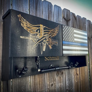 May include: A black wooden wall mounted key holder with a gold eagle emblem, a thin blue line American flag, and the name "Schmidt" engraved below.