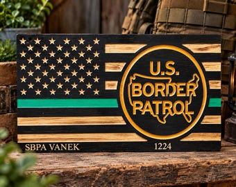 May include: A rectangular wooden sign featuring a carved American flag design with black and natural wood stripes, a green horizontal line, and a central circle containing a map outline and the text U.S. BORDER PATROL. SBPA VANEK and 1224 are engraved.