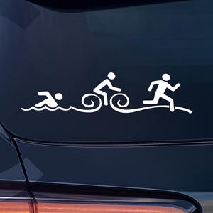 Può includere: Un adesivo in vinile bianco con una grafica stilizzata di una sequenza di triathlon. Il design mostra un nuotatore, un ciclista e un corridore in una linea continua, che rappresentano le tre fasi dello sport, applicato su una superficie scura.