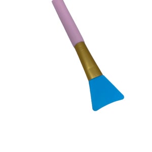 Pu&ograve; includere: Uno spazzolino per il viso in silicone con manico rosa e dorato e una testa triangolare blu.