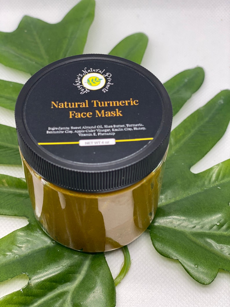 Pu&ograve; includere: Un barattolo di vetro con un coperchio nero che contiene una maschera per il viso naturale al curcuma. Il barattolo &egrave; etichettato "Natural Turmeric Face Mask" e elenca gli ingredienti: olio di mandorle dolci, burro di karit&egrave;, curcuma, argilla bentonite, aceto di sidro di mele, argilla caolino, miele, vitamina E, fenossietanolo. Il barattolo &egrave; appoggiato su una foglia verde.