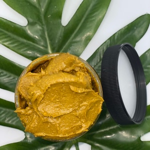 Pu&ograve; includere: Un barattolo di vetro pieno di una sostanza densa, di colore marrone dorato e cremosa. Il barattolo &egrave; sopra una foglia verde.