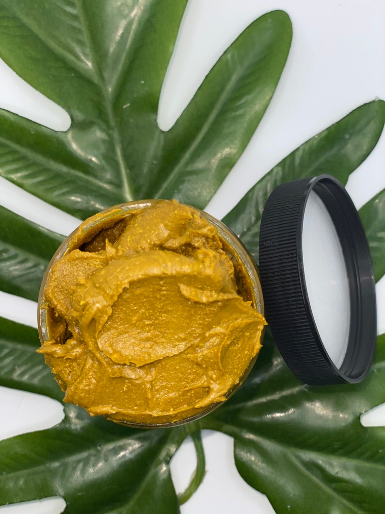 Pu&ograve; includere: Un barattolo di vetro pieno di una sostanza densa, di colore marrone dorato e cremosa. Il barattolo &egrave; sopra una foglia verde.