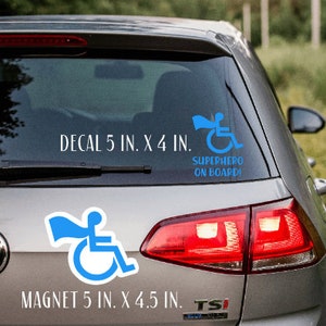 Pode incluir: Um carro prateado com um adesivo de super-her&oacute;i em cadeira de rodas azul na janela traseira. O adesivo diz "SUPERHERO ON BOARD". Abaixo do adesivo, h&aacute; um texto branco que diz "DECAL 5 IN. X 4 IN.". Um &iacute;m&atilde; de super-her&oacute;i em cadeira de rodas azul est&aacute; na parte inferior esquerda da janela traseira. O &iacute;m&atilde; diz "MAGNET 5 IN. X 4.5 IN."