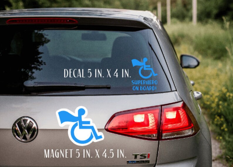 Pode incluir: Um carro prateado com um adesivo de super-her&oacute;i em cadeira de rodas azul na janela traseira. O adesivo diz "SUPERHERO ON BOARD". Abaixo do adesivo, h&aacute; um texto branco que diz "DECAL 5 IN. X 4 IN.". Um &iacute;m&atilde; de super-her&oacute;i em cadeira de rodas azul est&aacute; na parte inferior esquerda da janela traseira. O &iacute;m&atilde; diz "MAGNET 5 IN. X 4.5 IN."