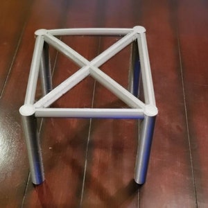 May include: A white metal stand with four legs and a criss-cross design. The stand is made of metal tubing and has a square base.
