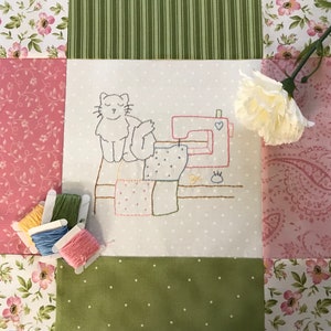 May include: A handmade quilt square featuring an embroidered cat with a sewing machine. The design includes spools of thread in various colors and a white carnation. The quilt has floral and striped fabric patterns.
