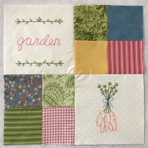 以下が含まれることがあります： ピンク色のスクリプトで「garden」の文字が刺繍され、緑のつるで縁取られたパッチワークのキルト正方形。正方形には、花柄、水玉模様、ストライプ、ニンジンの刺繍など、さまざまな生地のパターンが使用されています。