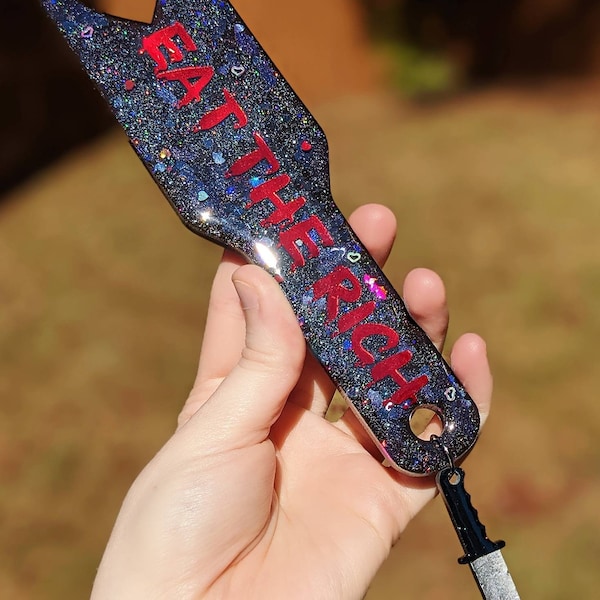 Eat the Rich red and black holo glitter with red foil resin heart cutout paddle with knife charm.