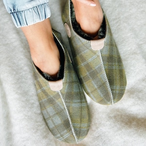 May include: A pair of green and blue plaid slippers with a fluffy lining. The slippers are made from a soft, comfortable material and have a relaxed fit.