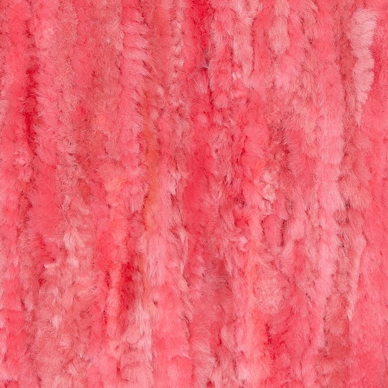 May include: Close-up of a vibrant, textured, coral-colored fabric. The material has a soft, plush appearance with vertical, slightly irregular lines, creating a sense of depth and dimension. The overall effect is warm and inviting.